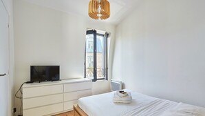 Een slaapkamer met een bed, een televisie op een dressoir, een raam met gordijnen en een plafondlamp.