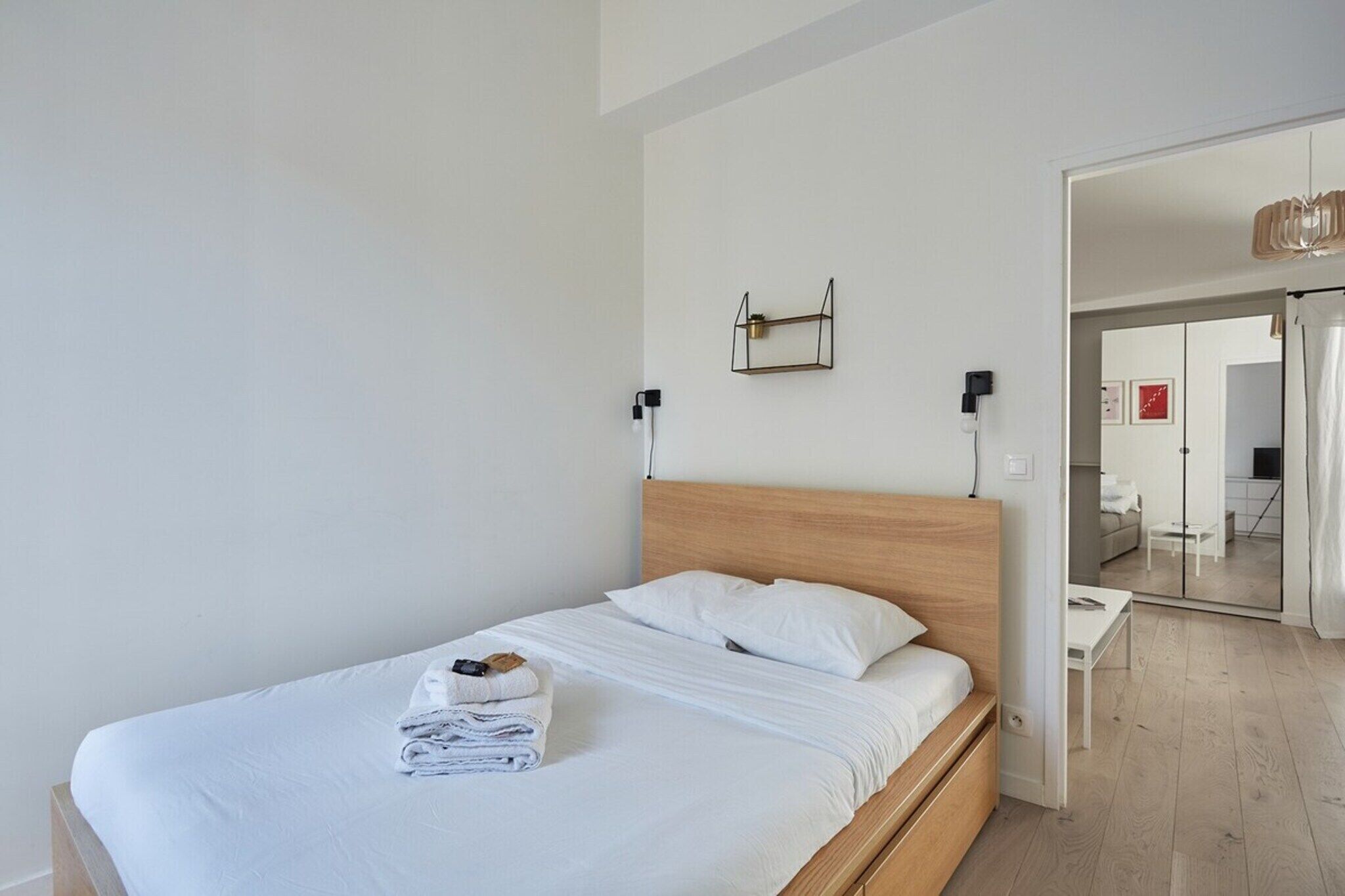 A modern hotel room with a wooden bed, white bedding, and a small bedside table with a lamp.