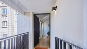 Een smalle gang met een zwarte deur die naar een kamer leidt, een houten vloer en een klein tapijt bij de ingang.