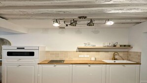 A kitchen with white cabinets, a wooden countertop, a built-in oven, a sink with a gold faucet, and three pendant lights. - Apartment Saint Germain des Pres Bon Marche (Paris)