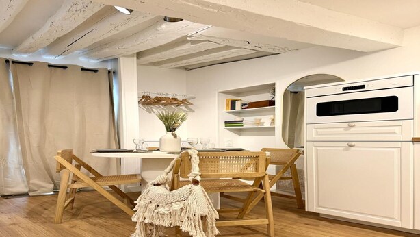 A room with a wooden dining table, two wooden chairs, a white cabinet, and a ceiling with exposed beams. - Apartment Saint Germain des Pres Bon Marche (Paris)