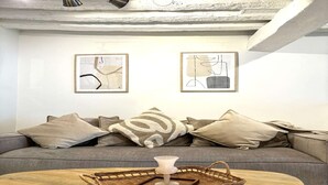 A modern living room with a grey sofa, two abstract wall art pieces, a white vase on a wooden table, and a woven basket. - Apartment Saint Germain des Pres Bon Marche (Paris)