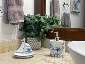 Ein Badezimmer mit Marmorplatte, einer Topfpflanze, einer dekorativen Seifenspender und einem kleinen Segelbootmodell.