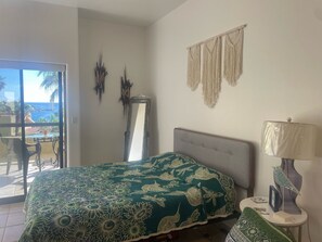 Ein Schlafzimmer mit einem Bett, einem Nachttisch, einer Lampe, einem Spiegel und Blick ins Freie.