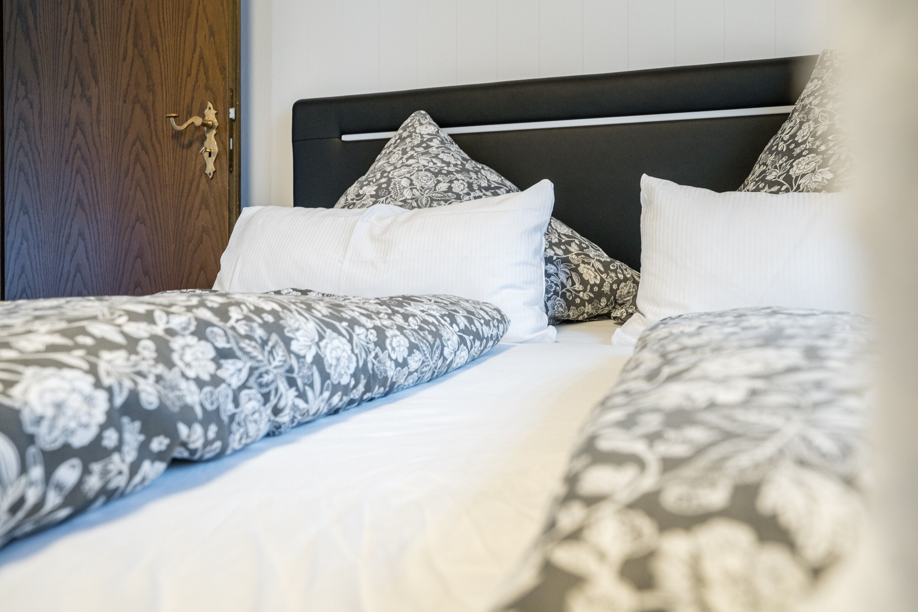 A bed with patterned bedding, a wooden door, and a headboard with a horizontal bar.
