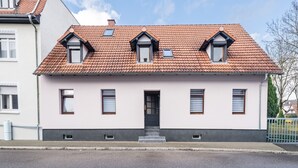 Ein zweistöckiges Gebäude mit einem Ziegeldach, einem zentralen Eingang und zwei kleinen Fenstern im oberen Stockwerk.