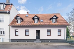 Un bâtiment à deux étages, doté d’un toit recouvert de tuiles, d’une entrée centrale et de deux petites fenêtres à l’étage supérieur.