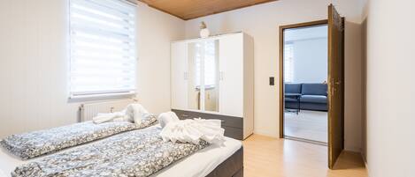 Un dormitorio con cama, armario, espejo y puerta que da a una sala de estar.