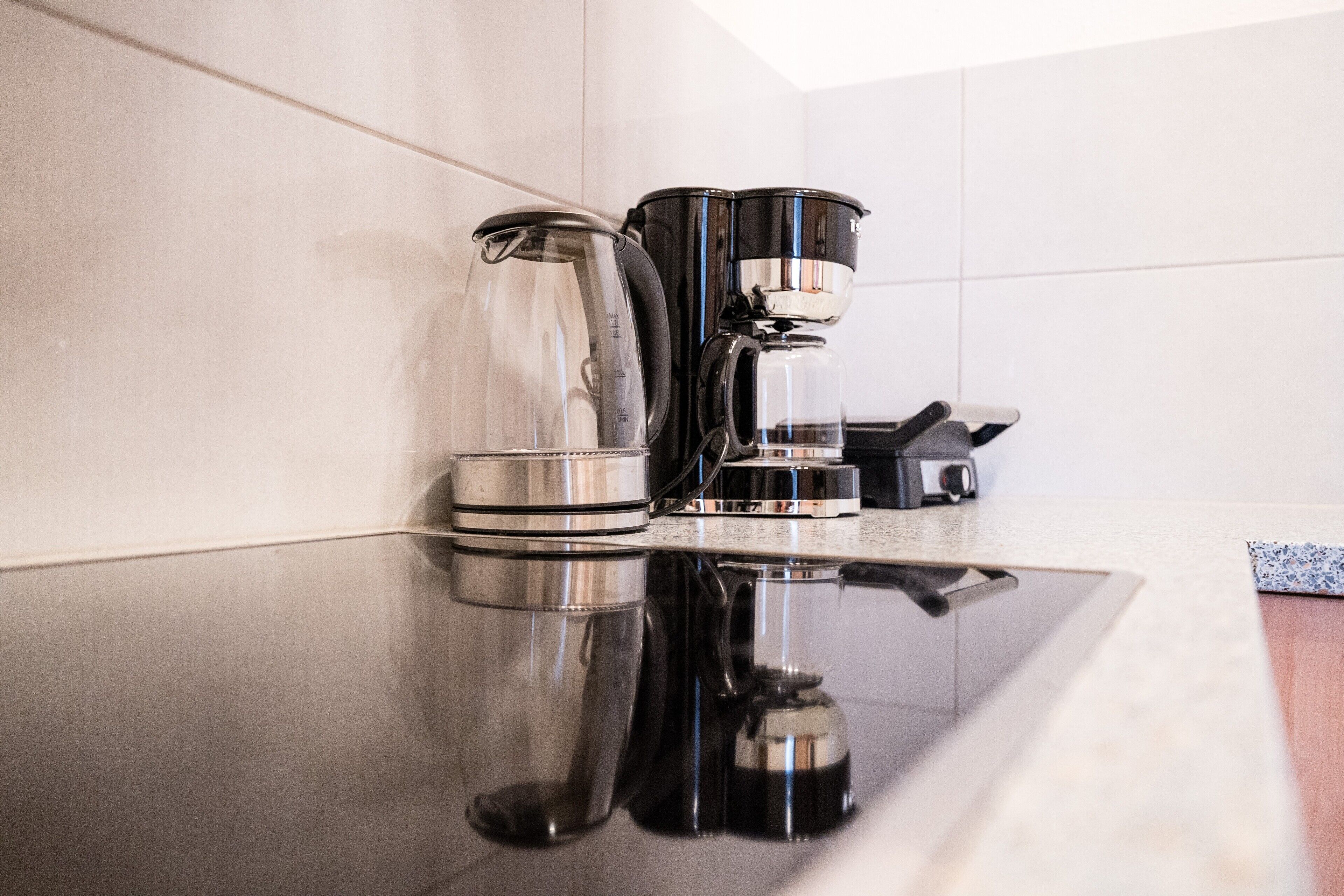 Une cuisine moderne équipée d’une machine à café, d’une verseuse en verre et d’une bouilloire, le tout posé sur un plan de travail réfléchissant.