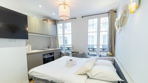 A modern hotel room with a bed, bedside table, and a view of the city through large windows.