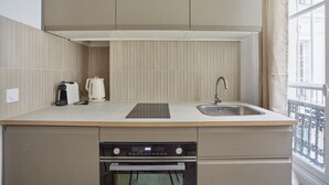 A compact kitchen with a built-in oven, a sink, and a kettle on the countertop.
