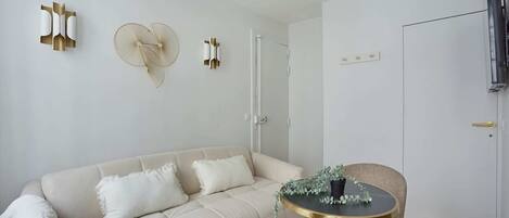 A modern living room with a beige sofa, a round table with a plant, and wall-mounted light fixtures.