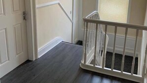 A staircase with a white railing, a door, and a window with blinds. - 5 Bedroom Holiday House – Clarendon 65 (Wallasey)