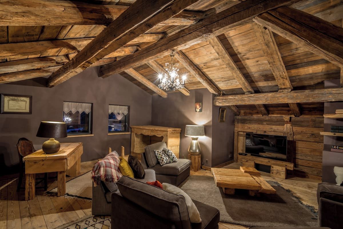 A rustic interior with exposed wooden beams, a fireplace, a sofa, a coffee table, and a television.
