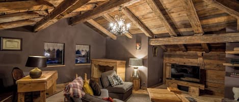 A rustic interior with exposed wooden beams, a fireplace, a sofa, a coffee table, and a television.
