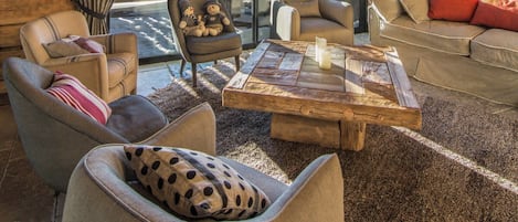 A log cabin interior with a large window, furnished with leather sofas and armchairs, a wooden coffee table, and a view of a snowy landscape.