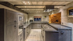 A modern kitchen with built-in appliances, a central island, and a rustic wooden wall. - Chalet La Roche du Renard - 300 m² chalet in Gérardmer, sauna (Gérardmer)