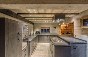 A modern kitchen with built-in appliances, a central island, and a rustic wooden wall. - Chalet La Roche du Renard - 300 m² chalet in Gérardmer, sauna (Gérardmer)