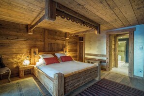 A wooden cabin bedroom with a bed, nightstand, and a view of the outside.