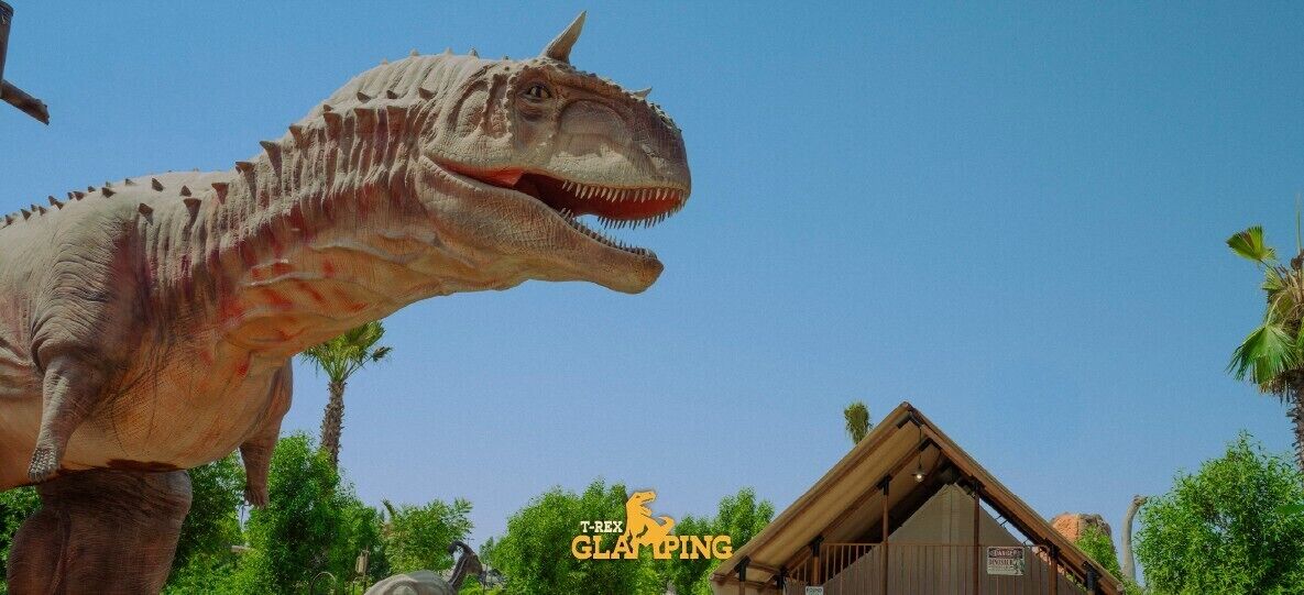Une grande statue de dinosaure dans un parc, avec un bâtiment en bois en arrière-plan.