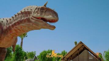 Une grande statue de dinosaure dans un parc, avec un bâtiment en bois en arrière-plan.