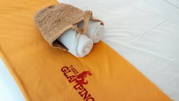 A bed with a rolled white towel and a brown head covering on an orange towel with a logo.
