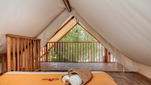 A bedroom with a bed, a wooden railing, and a view of trees through a window. - T-Rex Glamping, Dubai Parks and Resorts (Dubai)