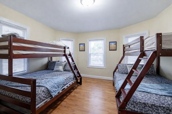 Quarto com duas beliches, piso de madeira e janelas com cortinas.