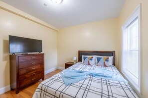 Quarto com cama, penteadeira, televisão em cima e janela com persianas.