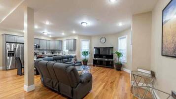 A modern living room with a sectional sofa, a flat-screen TV, and a dining area with a glass table.