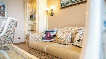 Een gezellige woonkamer met een bloemenbank, een gestreept kussen en een wandplank met boeken.