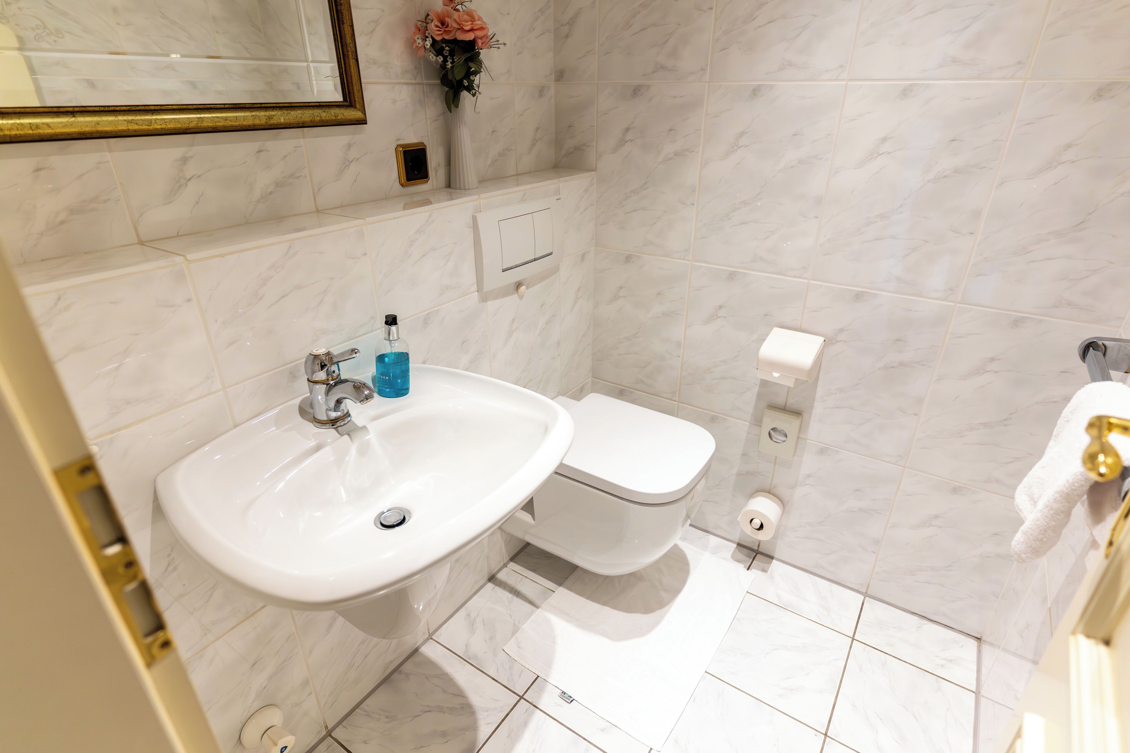 A bathroom with a white sink, toilet, and marble tiles.