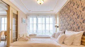 Quarto de hotel com uma cama grande, um espaço de estar com uma poltrona e vista pela janela.