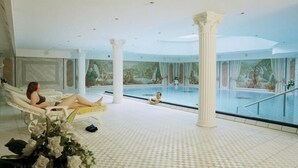 Uma área interna de piscina ampla, com uma piscina grande, uma espreguiçadeira e um pilar decorativo.