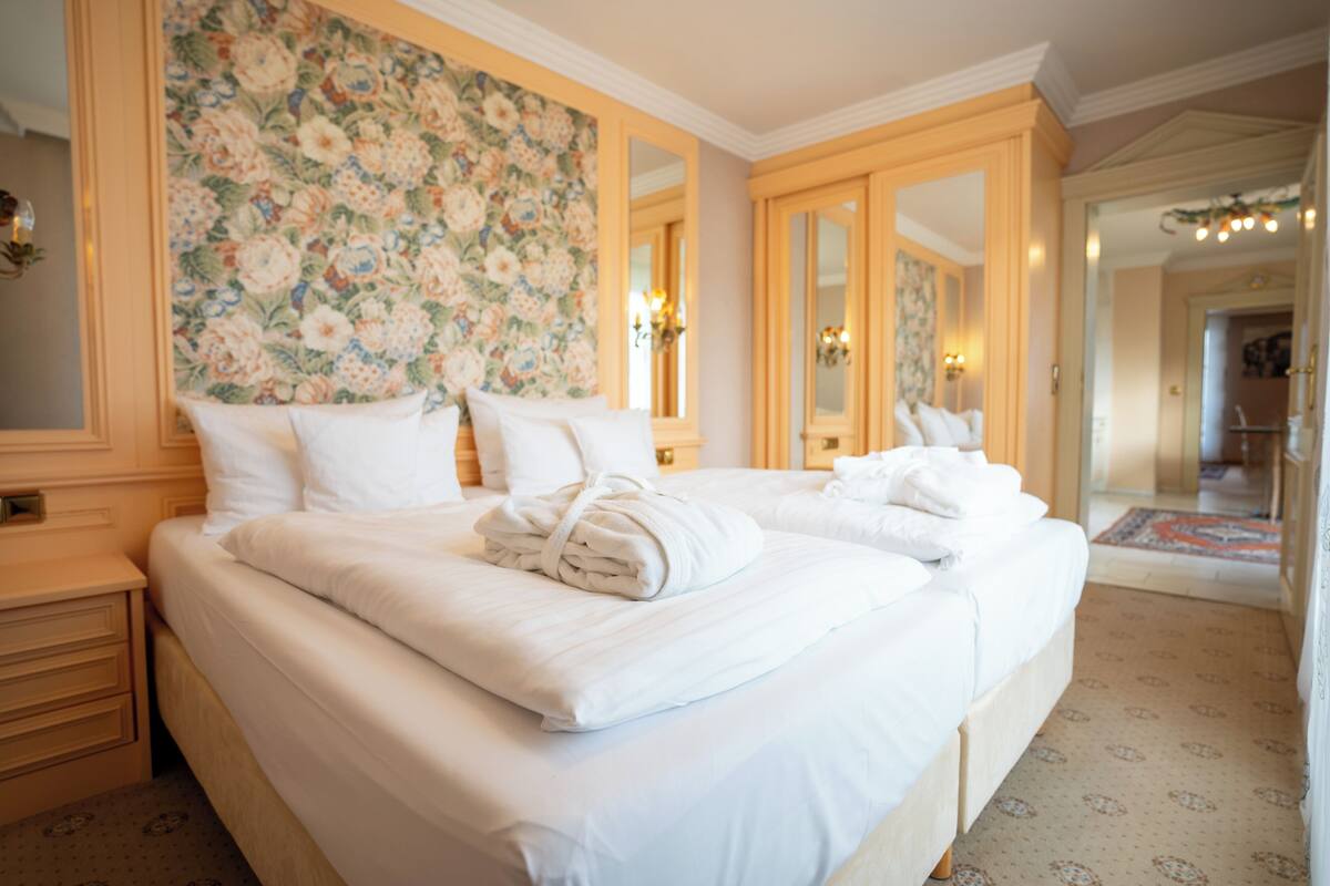 Ein Hotelzimmer mit einem großen Bett, blumigem Wandpapier und einem Spiegel.