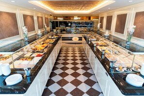 A buffet area with a checkered floor, glass display cases with food, and a bar in the background. - Seeschlößchen (Cuxhaven)