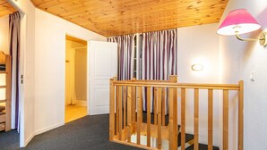Une pièce avec un plafond en bois, une porte blanche, un rideau à rayures et une petite balustrade en bois.
