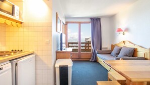 Une pièce compacte comprenant un coin cuisine, un lit et une vue sur les montagnes par la fenêtre.