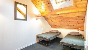 Une petite chambre accueillante avec deux lits simples, un plafond en bois et une lucarne.