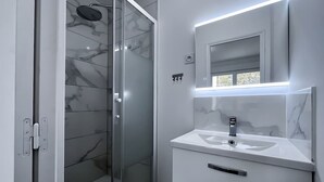 A modern bathroom with a glass-enclosed shower, a white sink with a mirror, and marble tiles.