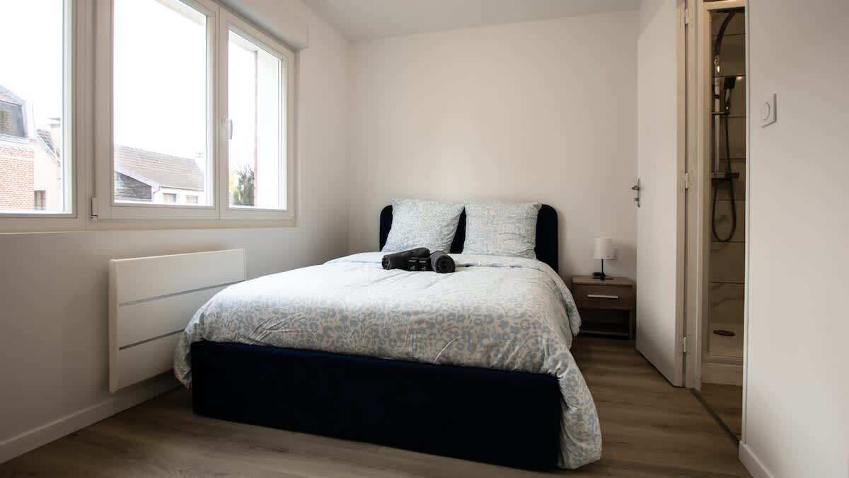Un dormitorio con cama, mesita de noche, lámpara y ventana.