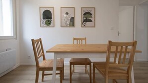 A dining area with a wooden table and four chairs, three framed artworks on the wall, and a white door in the background.