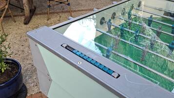 A foosball table in an outdoor patio area with a stone wall and potted plants.