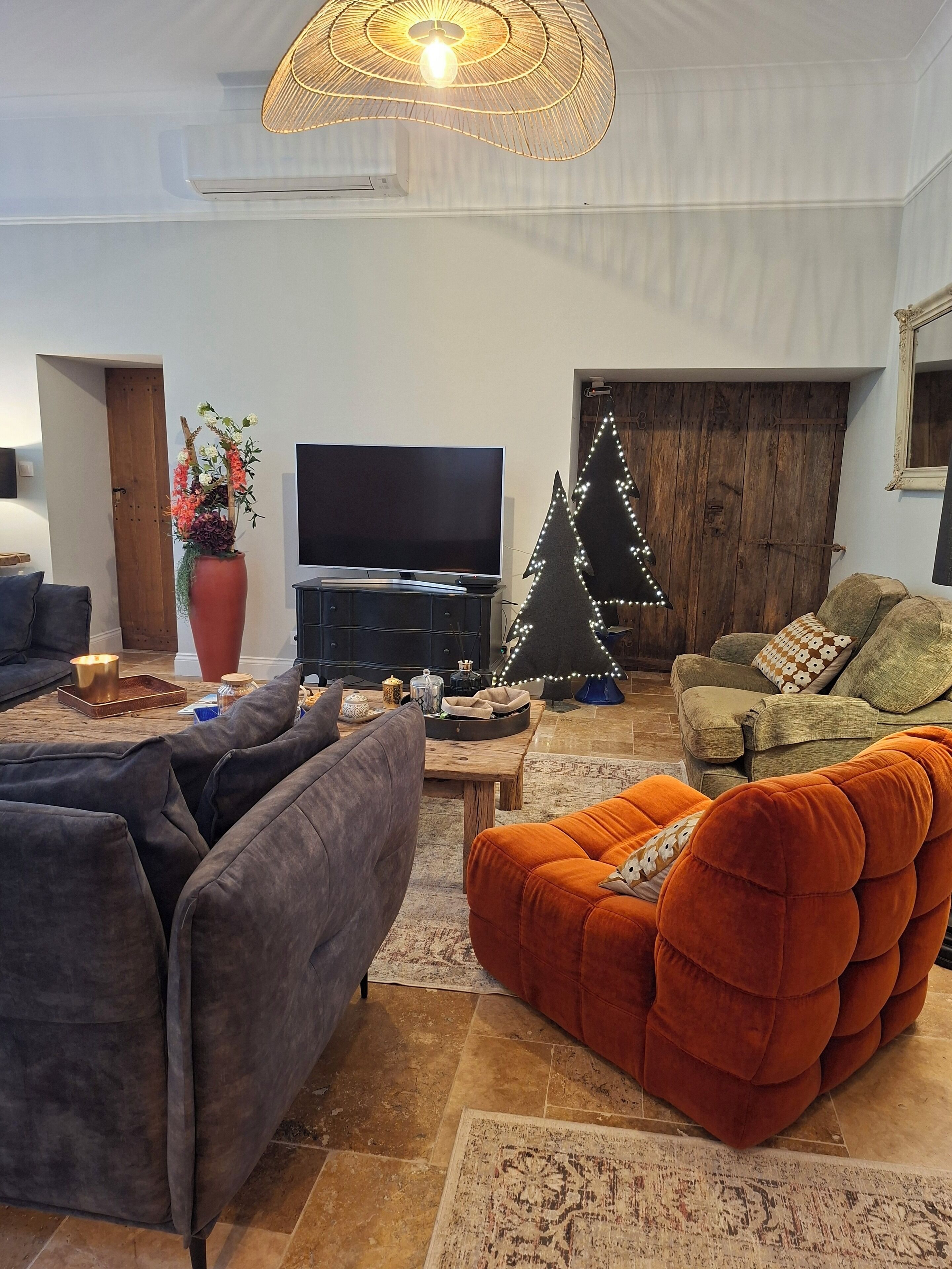 A living room with a sofa, a coffee table, a TV, a decorative tree, and a large window.