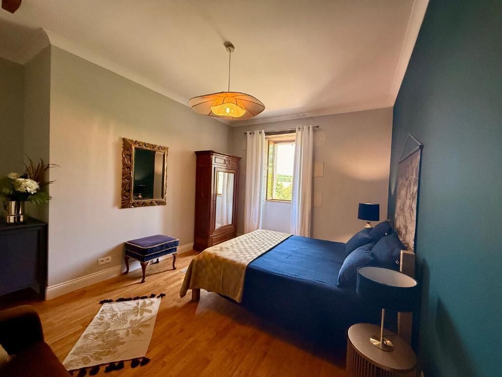 A bedroom with a bed, a bedside table, a lamp, a mirror, a wardrobe, and a window with curtains.