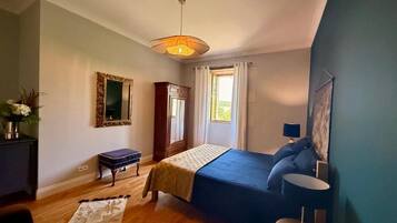 A bedroom with a bed, a bedside table, a lamp, a mirror, a wardrobe, and a window with curtains.