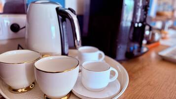 Una bandeja con cuatro tazas y platillos blancos, una cafetera y un hervidor sobre una mesa de madera.