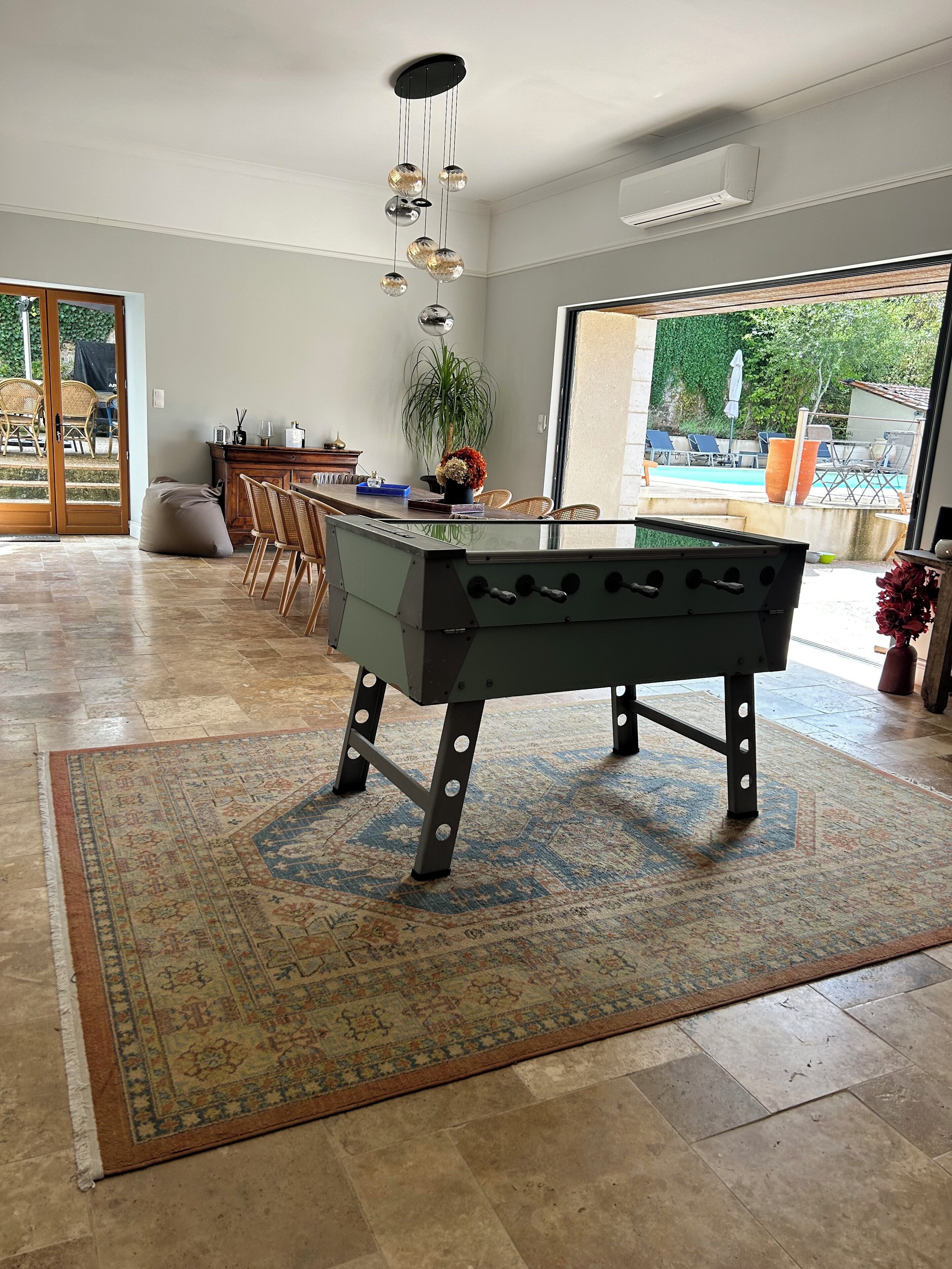 Amplo espaço interno com mesa de pebolim, mesa de jantar com cadeiras e vista para área externa com piscina.