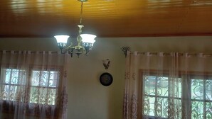 Une pièce avec un plafond en bois, deux fenêtres ornées de rideaux décoratifs, une horloge murale et un lustre.