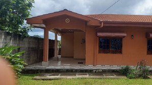 Une maison de plain-pied avec un toit en tuiles, une véranda et un petit jardin.